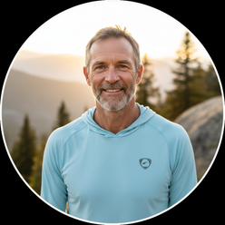 Circular portrait of Conrad Anker, a male climber, smiling confidently against a blurred mountain backdrop, wearing outdoor a